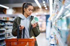 Young woman reads product label of yogurt in the grocery store.