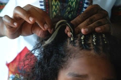 Hands braiding a young girls hair with blonde extensions.