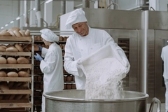 A worker pours bread baking ingredients into a large mixer in a bread factory.