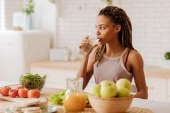 fit woman drinking water around fruit and vegetables on counter
