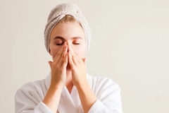 A woman with her hair in a towel and touching her face.