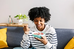 A woman eating fruit-filled yogurt on a couch.