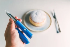 A person holding a GLP-1 medication injector in front of a donut.