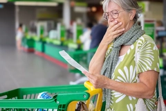 An older woman looks at her grocery receipt worriedly.