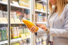 woman's hand holding orange juice bottle in supermarket