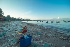 Image woman sits on beach surrounded by plastic packaging