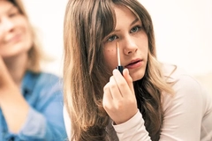 Image Girl applying her makeup in front of an adult and mirror