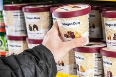 Human hand holding a pint of Haagen Dazs ice cream at a supermarket freezer.