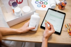 Image Hands holding supplement and package over pad on desk