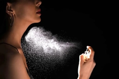 Woman spraying luxury perfume on black background.