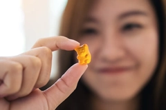 Asian woman smiling , holding and looking at orange gummy bear