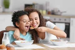 Image A young mother feeds her child some breakfast cereal at the kitchen table.