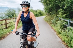 Portrait of a happy smiling woman dressed in cycling clothes, helmet and sunglasses riding a bicycle on the asphalt out-of-town bicycle path.