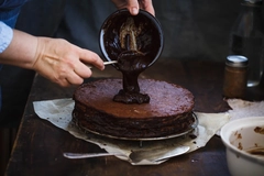 Chef's hand spreading chocolate ganache glazed over torte.