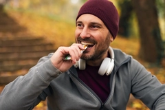 Image Happy man in beanie eating nutrition bar in park