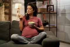 Image pregnant woman eating on the couch