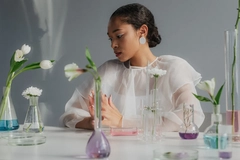 A woman with beakers and plants in front of her.