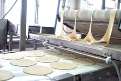Production line pizza dough stretching in a machine.