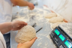 Bakers shaping raw bread dough by hand on floured table in bakery kitchen.