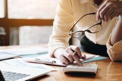 Image person uses calculator, holding glasses in hand