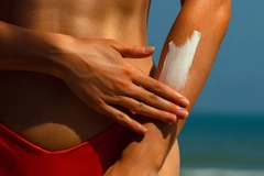 Image Woman applying sun screen to her arm on the beach