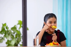 smiling girl snacking on paprika at table